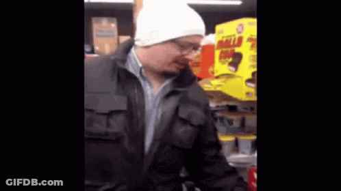 A Man Wearing A White Hat And A Black Jacket Is Standing In Front Of A Yellow Box That Says Hello Kitty GIF