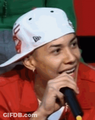 A Man Wearing A White Hat And A Red Jacket Is Holding A Microphone And Smiling . GIF