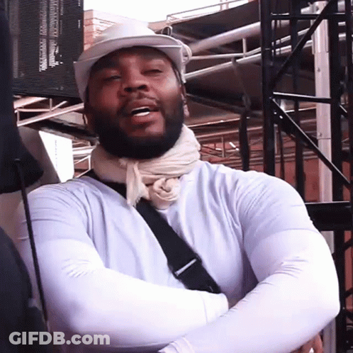 A Man Wearing A White Hat And A Scarf Around His Neck Is Standing With His Arms Crossed GIF