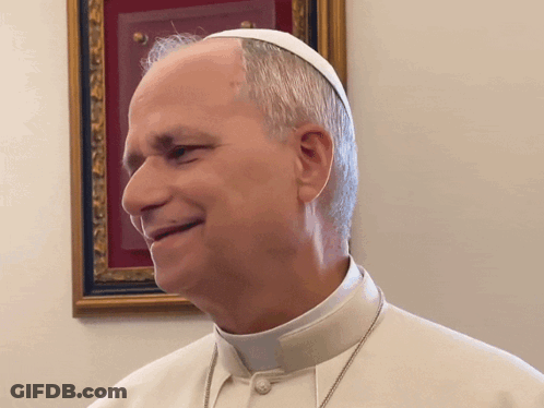 A Man Wearing A White Hat And Collar Is Smiling In Front Of A Framed Picture GIF