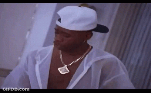 A Man Wearing A White Hat And Necklace Is Standing In A Room . GIF
