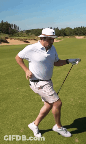 A Man Wearing A White Hat Is Holding A Golf Club On A Golf Course GIF