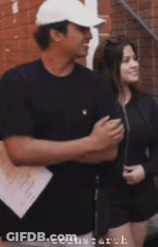 A Man Wearing A White Hat Is Standing Next To A Woman With The Word Arch On The Bottom Right GIF