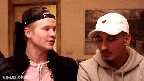 A Man Wearing A White Hat With A Red Heart On It Is Talking To Another Man . GIF