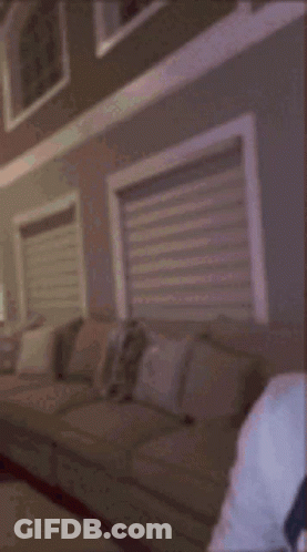 A Man Wearing A White Hoodie And Earbuds Is Sitting In Front Of A Window . GIF