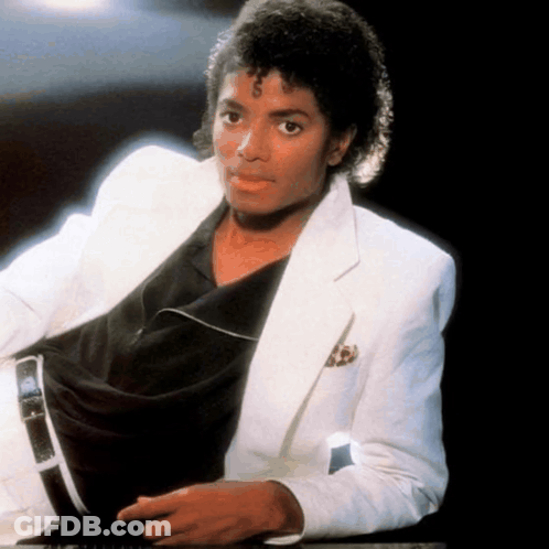 A Man Wearing A White Jacket And A Black Shirt Is Sitting Down GIF