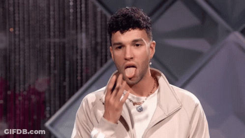 A Man Wearing A White Jacket And A Necklace Is Sticking His Tongue Out . GIF