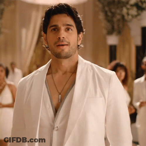 A Man Wearing A White Jacket And A Necklace Looks At The Camera GIF