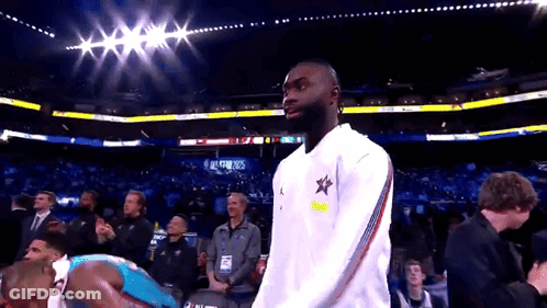 A Man Wearing A White Jacket With A Star On It Stands In A Stadium GIF