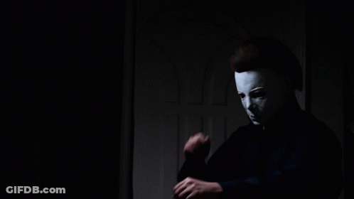 A Man Wearing A White Mask Is Standing In A Dark Room GIF