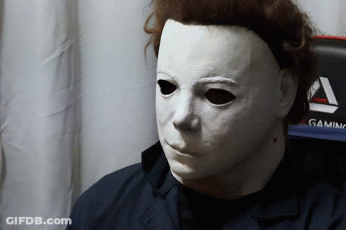 A Man Wearing A White Mask Stands In Front Of A Gaming Chair GIF