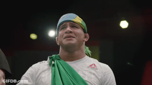 A Man Wearing A White Reebok Shirt With A Green Cloth Around His Neck GIF