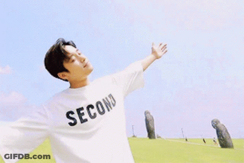 A Man Wearing A White Second T-Shirt Is Standing In A Field With His Arms Outstretched GIF