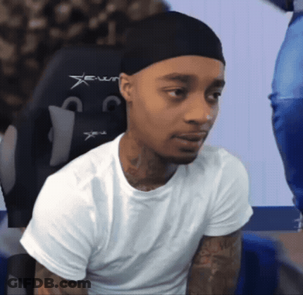 A Man Wearing A White Shirt And A Black Hat Is Sitting In A Chair . GIF