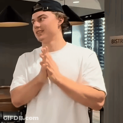 A Man Wearing A White Shirt And A Black Hat Is Standing In Front Of A Bistro Sign . GIF