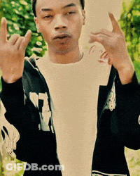 A Man Wearing A White Shirt And A Black Jacket With The Letter T On It Is Giving The Middle Finger GIF