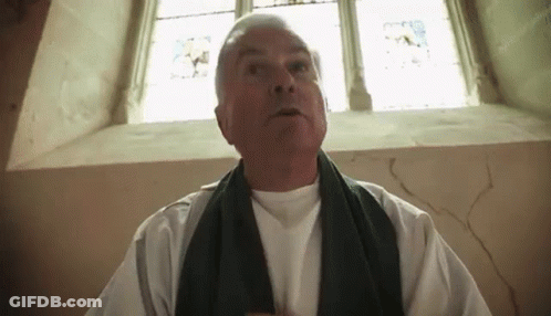 A Man Wearing A White Shirt And A Black Scarf Is Standing In Front Of A Window GIF