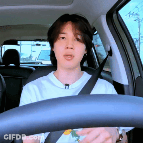 A Man Wearing A White Shirt And A Black Seat Belt Is Driving A Car GIF