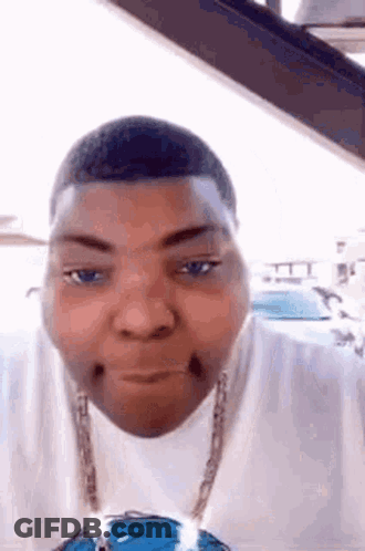 A Man Wearing A White Shirt And A Blue Necklace Is Making A Funny Face In A Car . GIF
