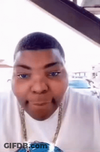 A Man Wearing A White Shirt And A Blue Necklace Is Making A Funny Face In A Car . GIF