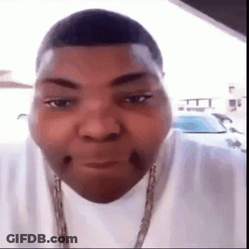 A Man Wearing A White Shirt And A Chain Around His Neck Is Making A Face . GIF