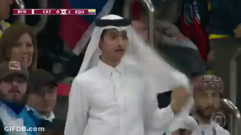 A Man Wearing A White Shirt And A Head Scarf Stands In A Crowd Watching A Soccer Game Between Cat And Equ GIF