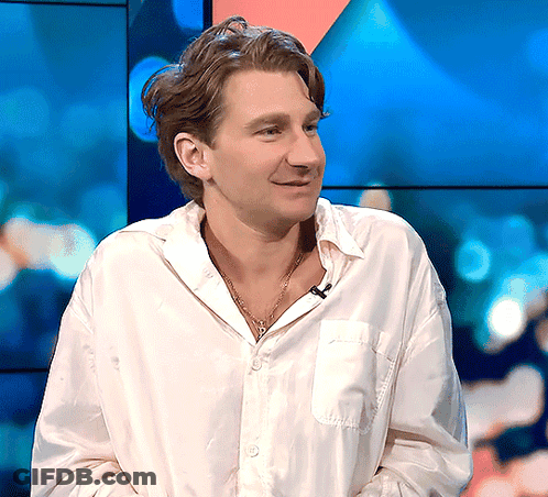 A Man Wearing A White Shirt And A Necklace Smiles GIF