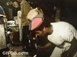 A Man Wearing A White Shirt And A Red Hat Is Kneeling Down In A Dark Room . GIF