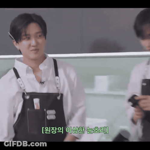 A Man Wearing A White Shirt And Black Apron Is Talking To Another Man GIF