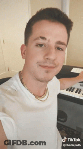 A Man Wearing A White Shirt And Gold Chain Is Standing In Front Of A Keyboard .. GIF