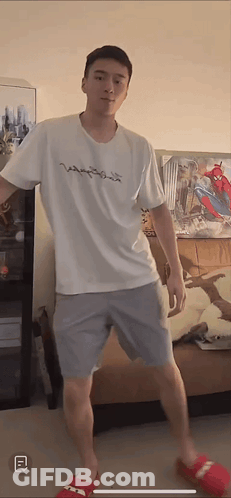 A Man Wearing A White Shirt And Grey Shorts Is Standing In A Living Room GIF