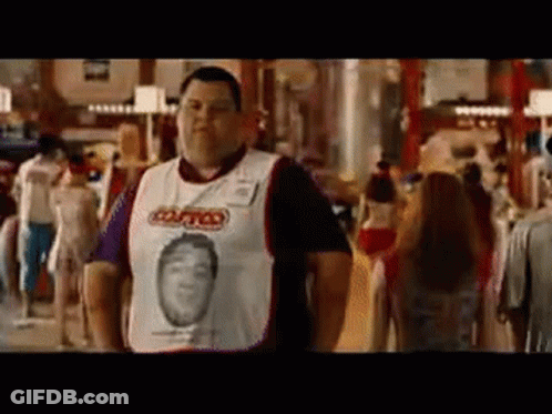A Man Wearing A White Shirt With A Picture Of A Man On It Is Standing In A Crowded Room . GIF