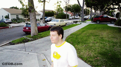 A Man Wearing A White Shirt With A Yellow Duck On It Walks Down The Sidewalk GIF