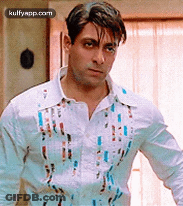 A Man Wearing A White Shirt With Paint Splattered On It Is Standing In Front Of A Window . GIF