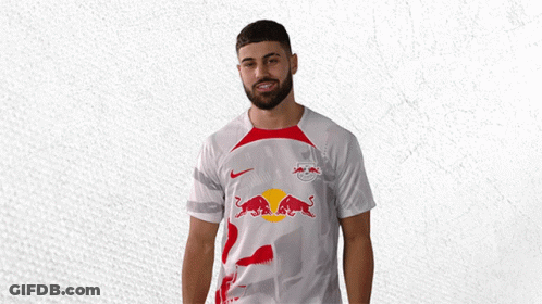 A Man Wearing A White Shirt With Red Bulls On It Is Waving GIF
