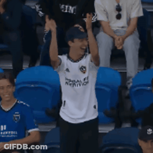 A Man Wearing A White Shirt With The Number 1 On It Stands In A Crowd GIF