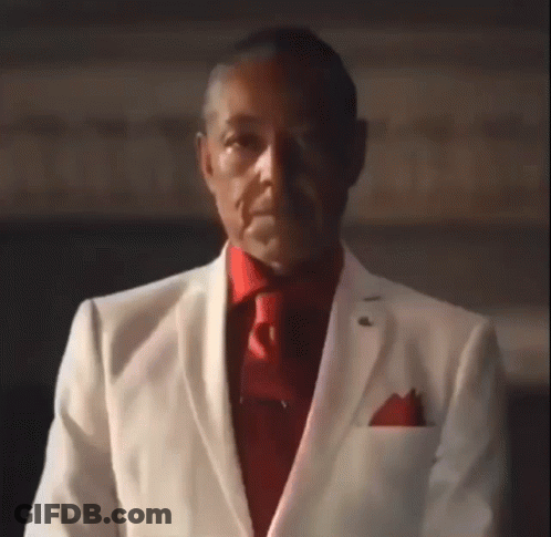 A Man Wearing A White Suit And Red Tie Is Looking At The Camera . GIF