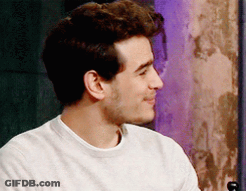 A Man Wearing A White Sweater Is Smiling And Looking To The Side GIF