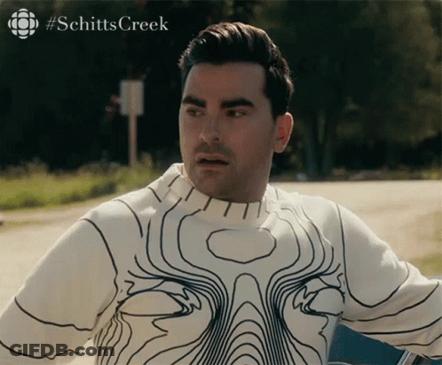 A Man Wearing A White Sweater With Black Lines And The Word Schitts Creek On The Bottom Right GIF