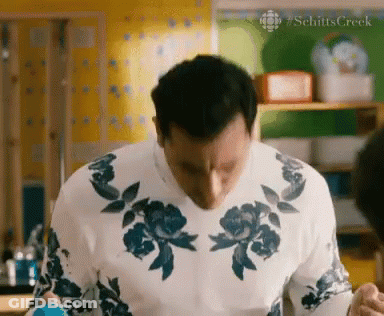 A Man Wearing A White Sweater With Blue Flowers On It Is Standing In A Kitchen GIF