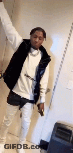A Man Wearing A White Sweatshirt And A Black Vest Is Standing In A Room With His Arms In The Air . GIF