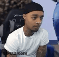 A Man Wearing A White T-Shirt And A Black Headband Is Sitting In A Chair . GIF