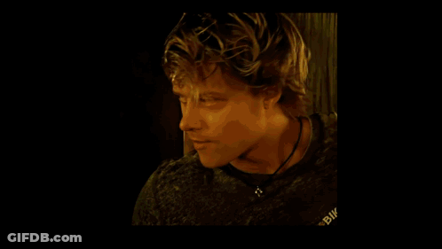 A Man Wearing A White T-Shirt Is Sitting In Front Of A Window Holding A Pair Of Gloves . GIF