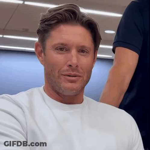 A Man Wearing A White T-Shirt Is Smiling For The Camera GIF