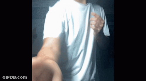A Man Wearing A White T-Shirt Is Standing In The Dark GIF