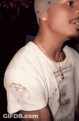 A Man Wearing A White T-Shirt With A Necklace Around His Neck And A Hat On GIF