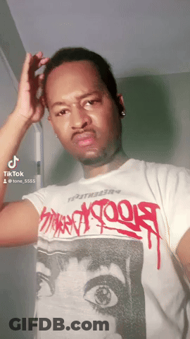A Man Wearing A White T-Shirt With Graffiti On It Is Looking At The Camera GIF