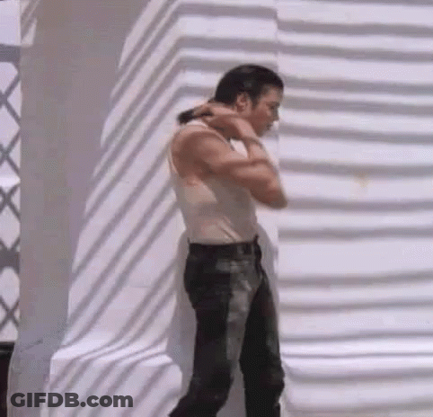 A Man Wearing A White Tank Top And Black Jeans Is Standing In Front Of A White Wall . GIF