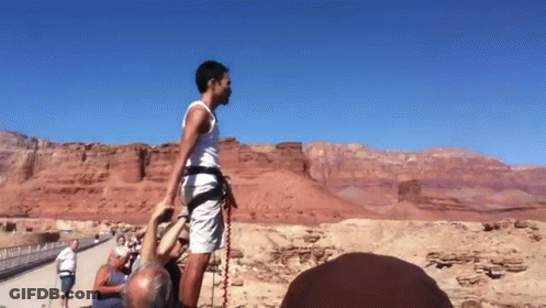 A Man Wearing A White Tank Top And Shorts Is Standing In Front Of A Desert Landscape GIF