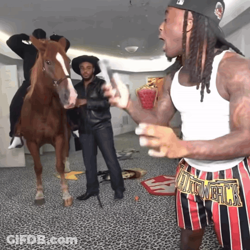 A Man Wearing A White Tank Top And Shorts That Say ' Tain Whack ' Stands In Front Of A Horse GIF